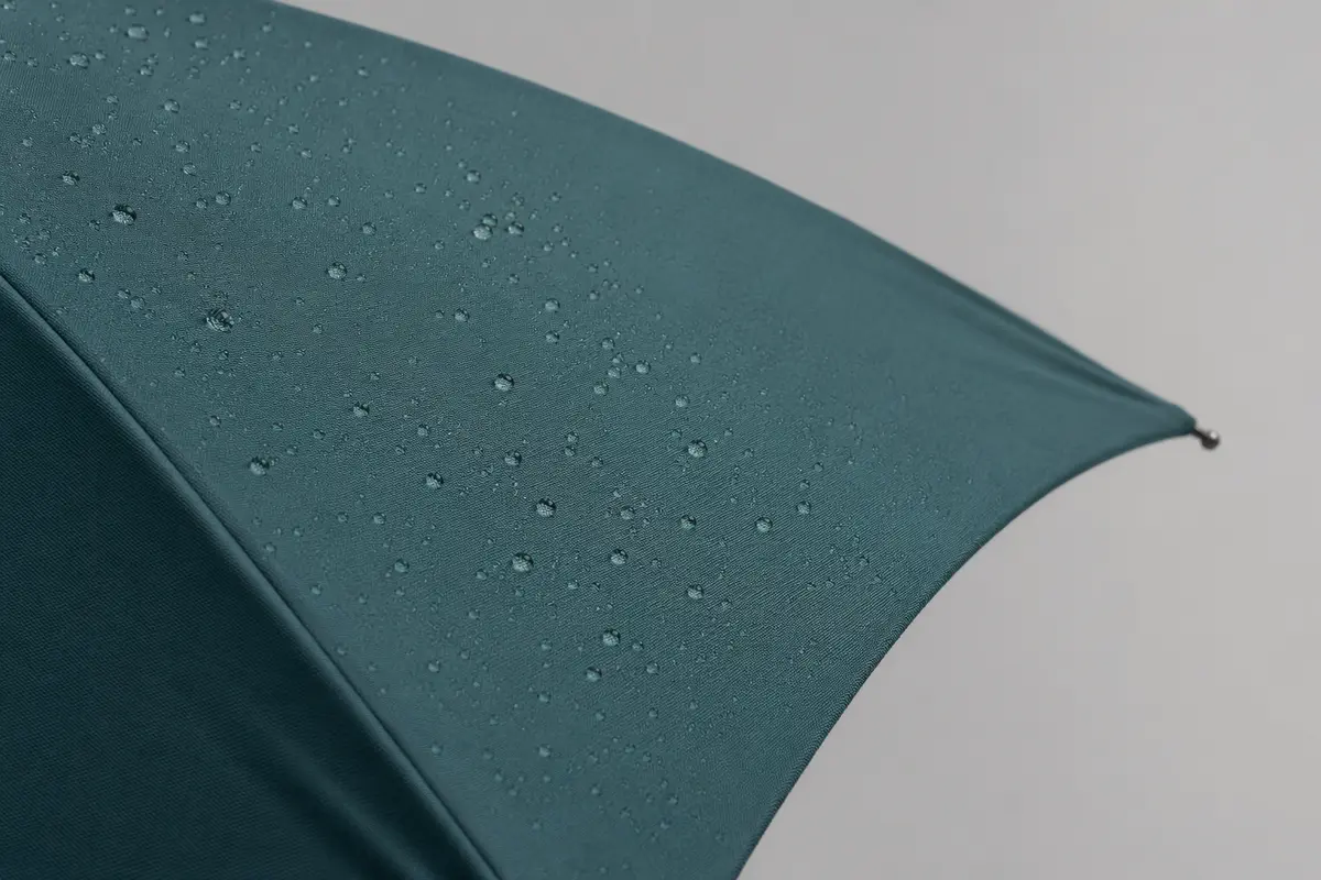 Close-up comparison image of dark teal polyester pongee umbrella canopy fabric with water droplets
