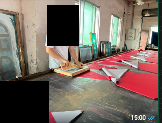A worker printing red umbrella panels on a long table, with identifying details redacted