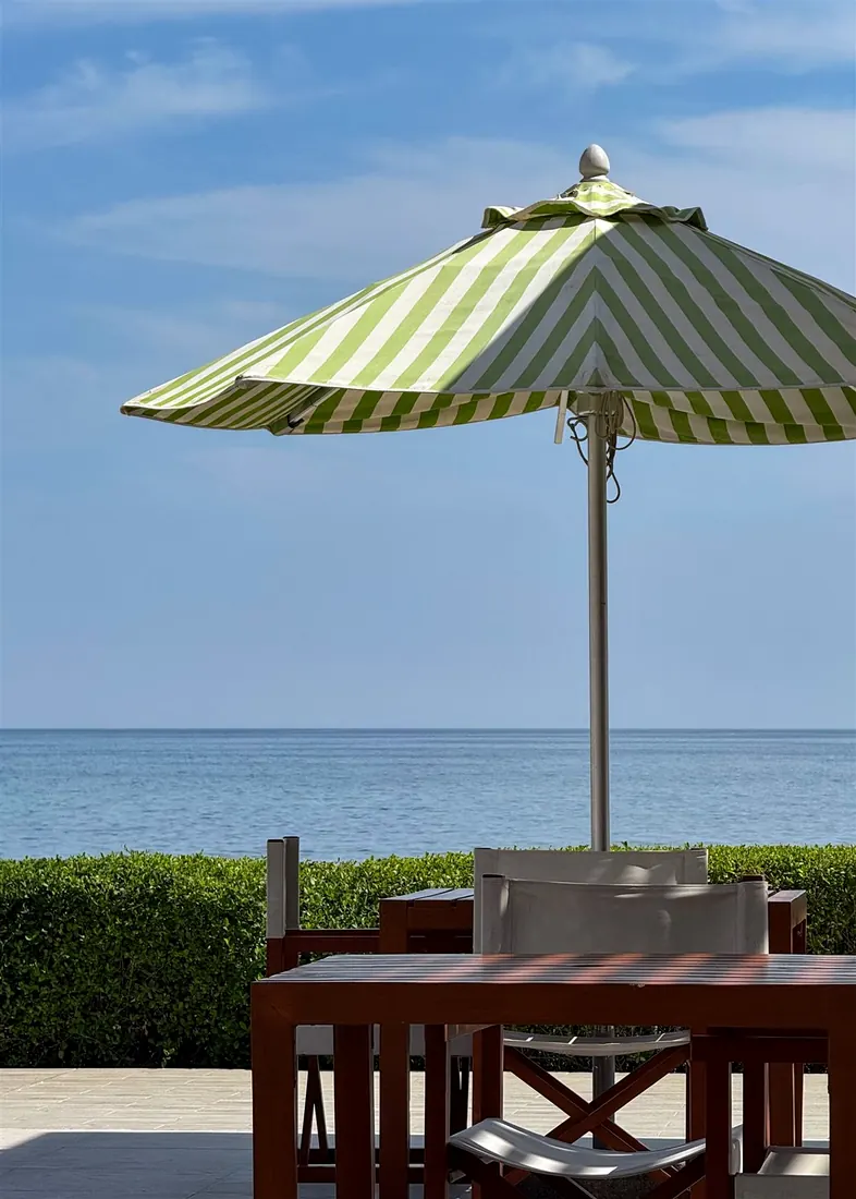 Striped patio umbrella used beside a hotel garden and seaside dining area