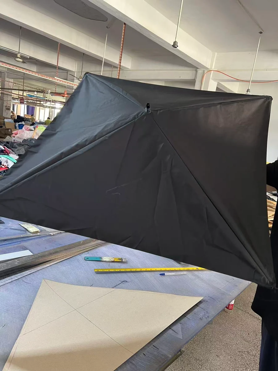 Black square umbrella sample above a workshop table with a cardboard pattern, ruler and cutting tools