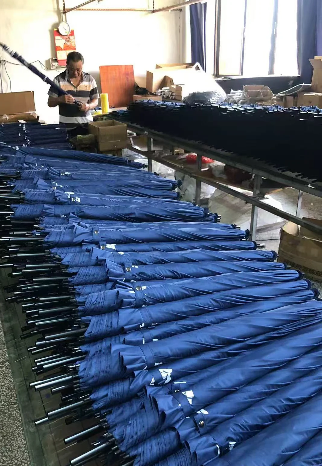 Umbrella factory workshop with a staff member holding an umbrella beside worktables with navy umbrellas.
